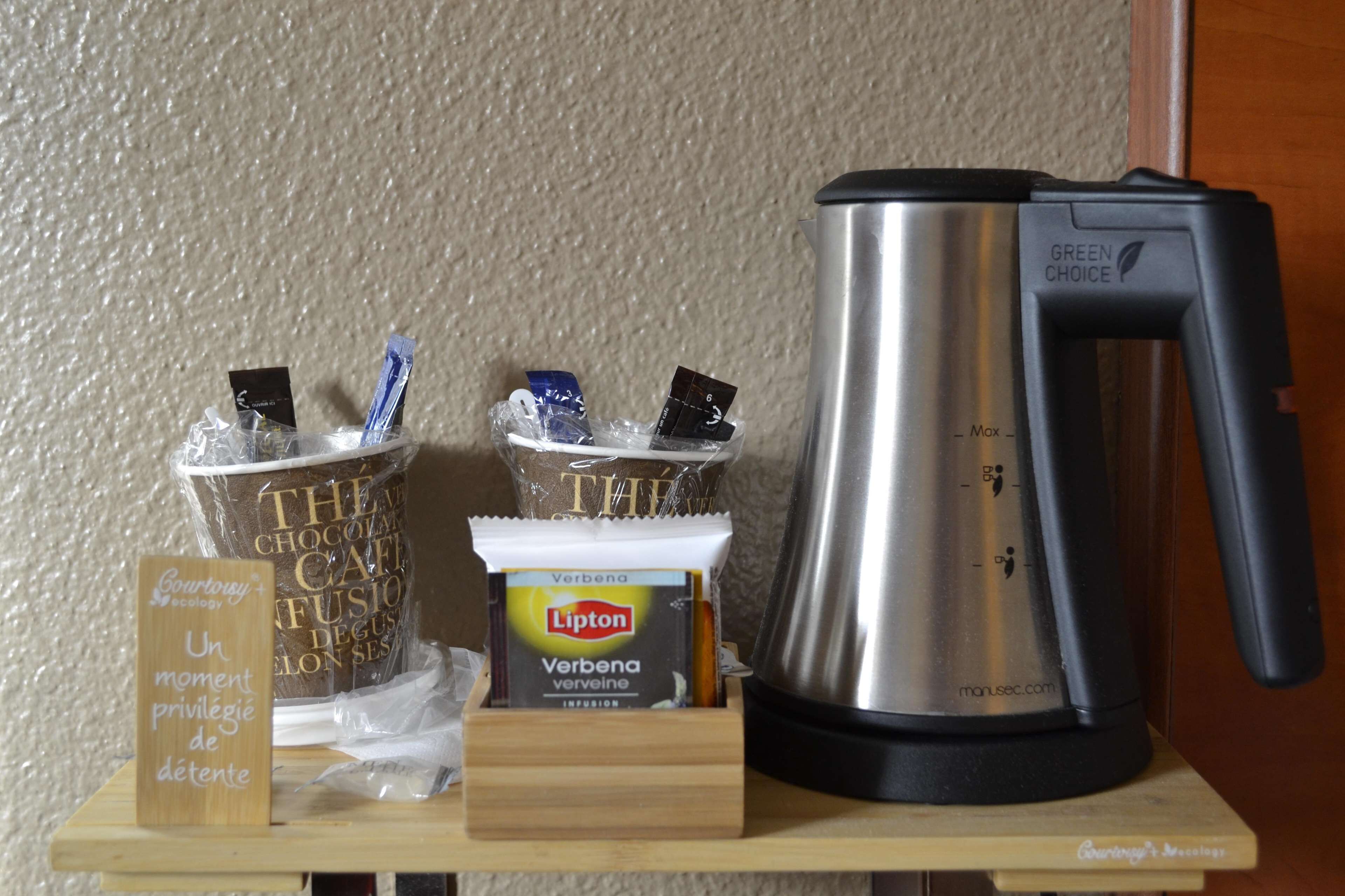 A coffee station with a coffee maker, cups, and a Lipton tea packet.