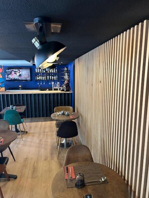 A restaurant interior with a bar area, wooden slat wall, and round tables. - Kyriad Brive La Gaillarde Centre (Brive-la-Gaillarde)