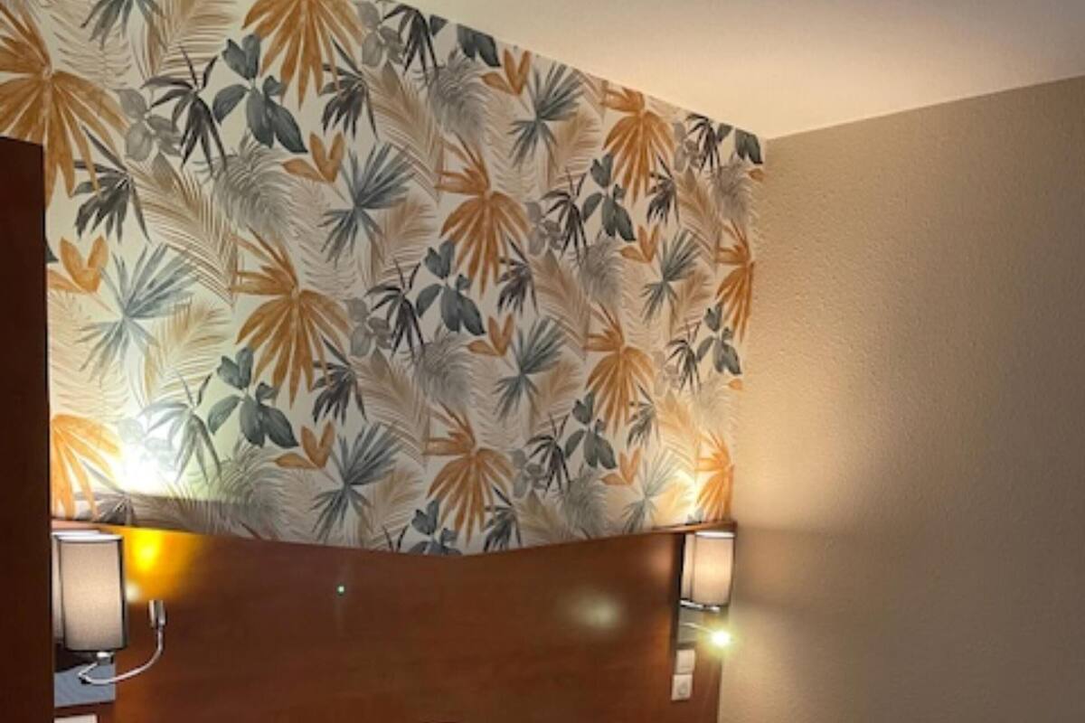 A hotel room with a bed, two bedside lamps, a nightstand, and a wall with a tropical leaf pattern.