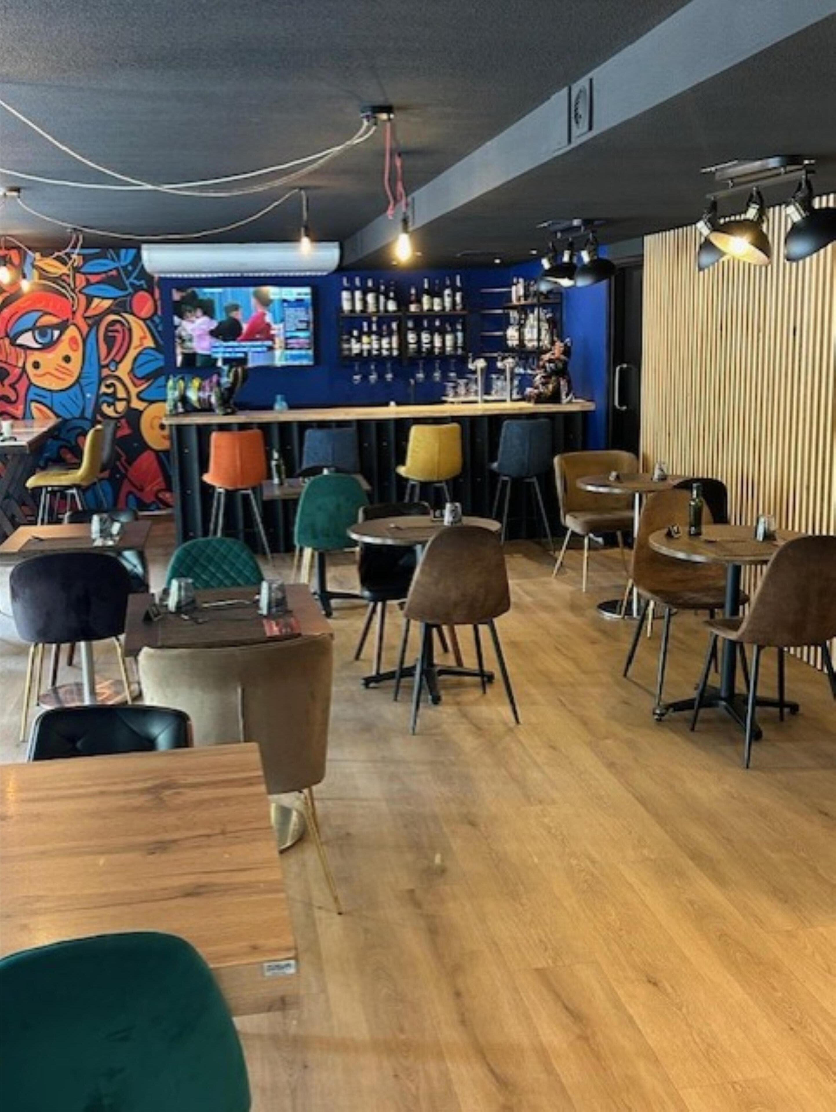 A restaurant interior with wooden tables and chairs, a bar area, and a colorful mural on the wall.