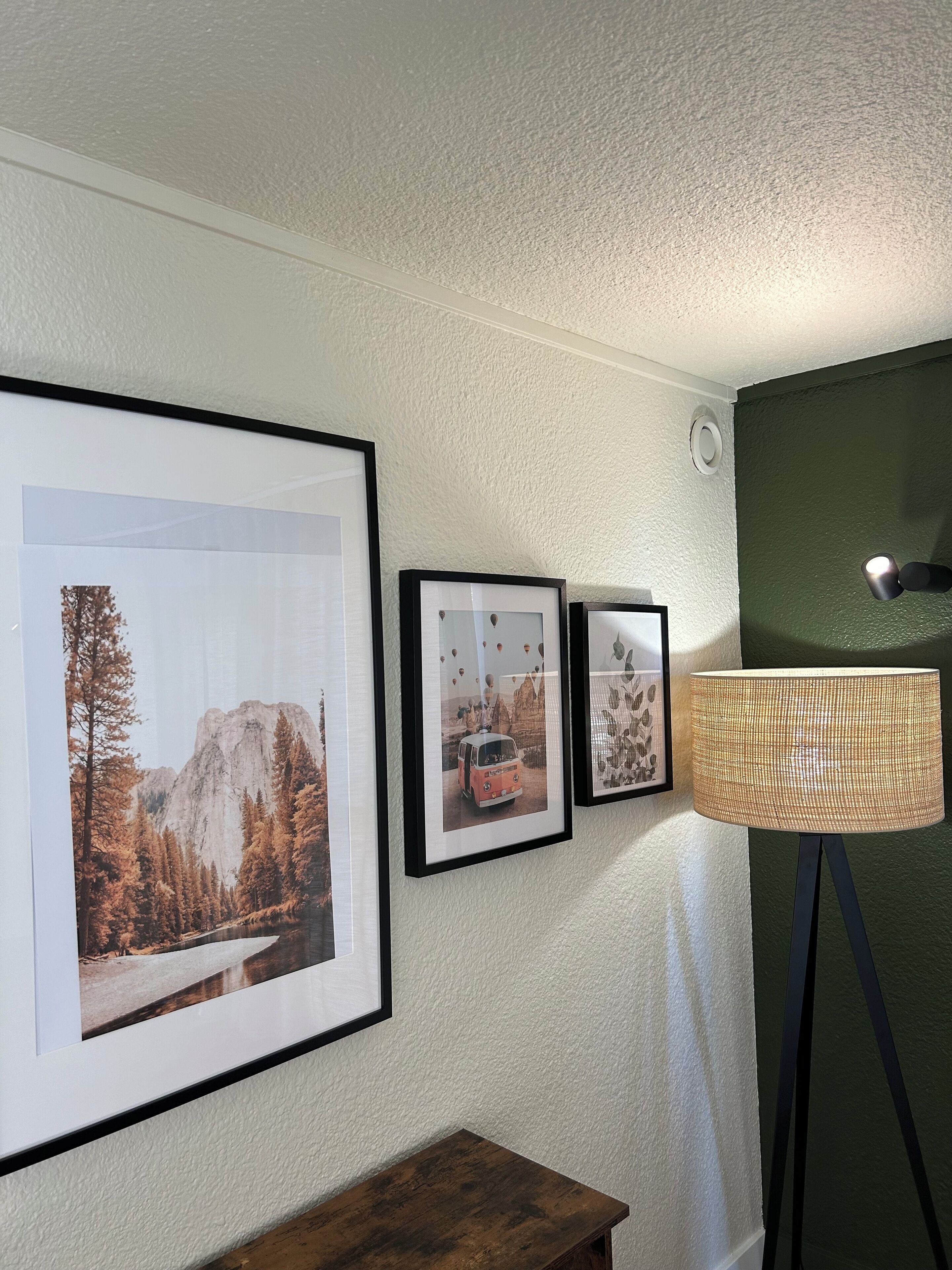 A room with framed pictures on the wall, a lamp, and a wooden table.
