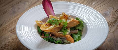 A white plate with a salad, bread, and a decorative purple element on a wooden table.