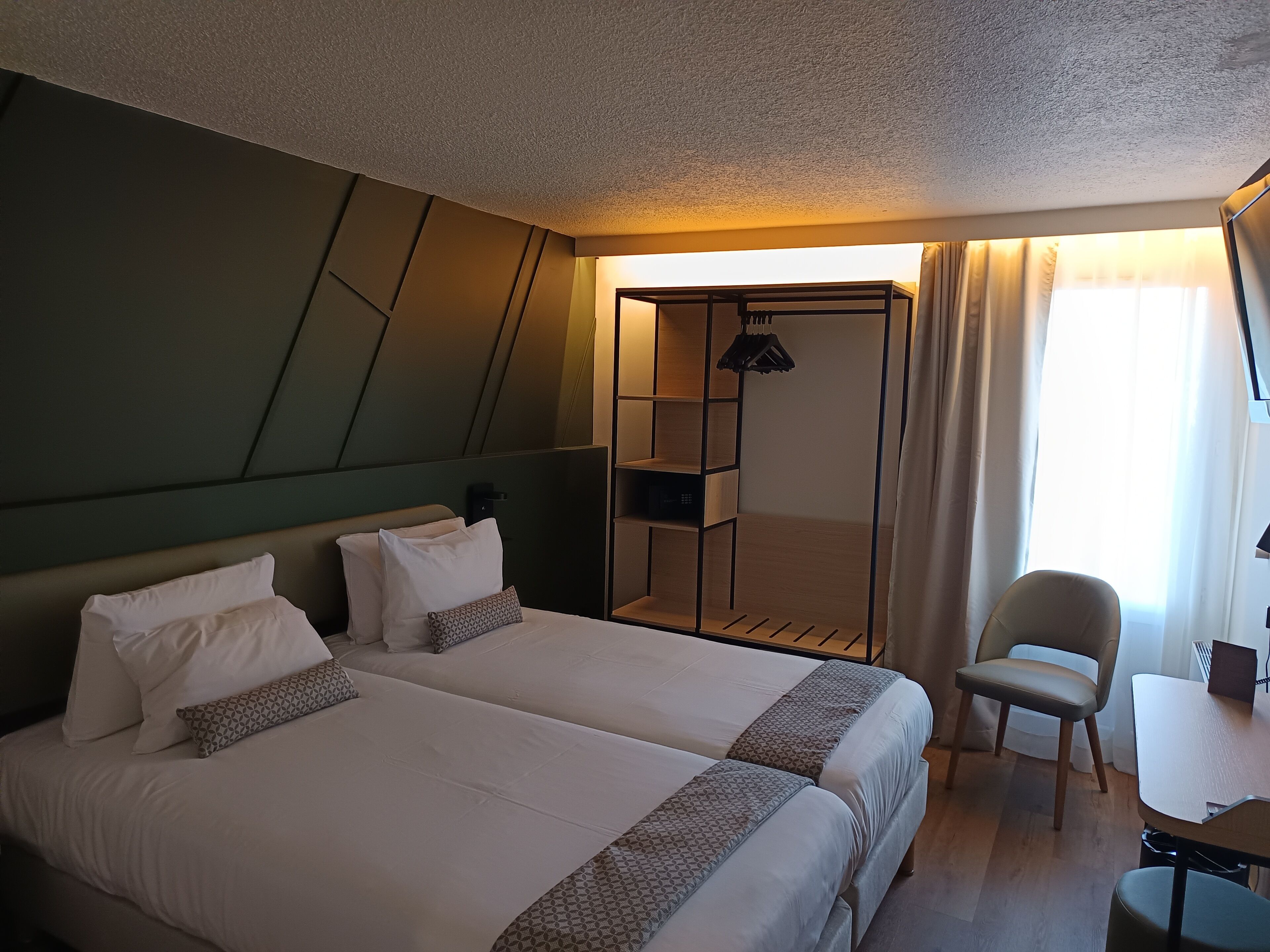 A hotel room with two beds, a desk, a chair, and a wardrobe.