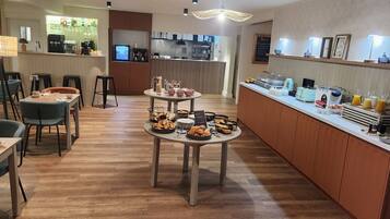 Un área de desayuno moderna con suelo de madera, una estación central de servicio y un espacio de estar con mesas y sillas.