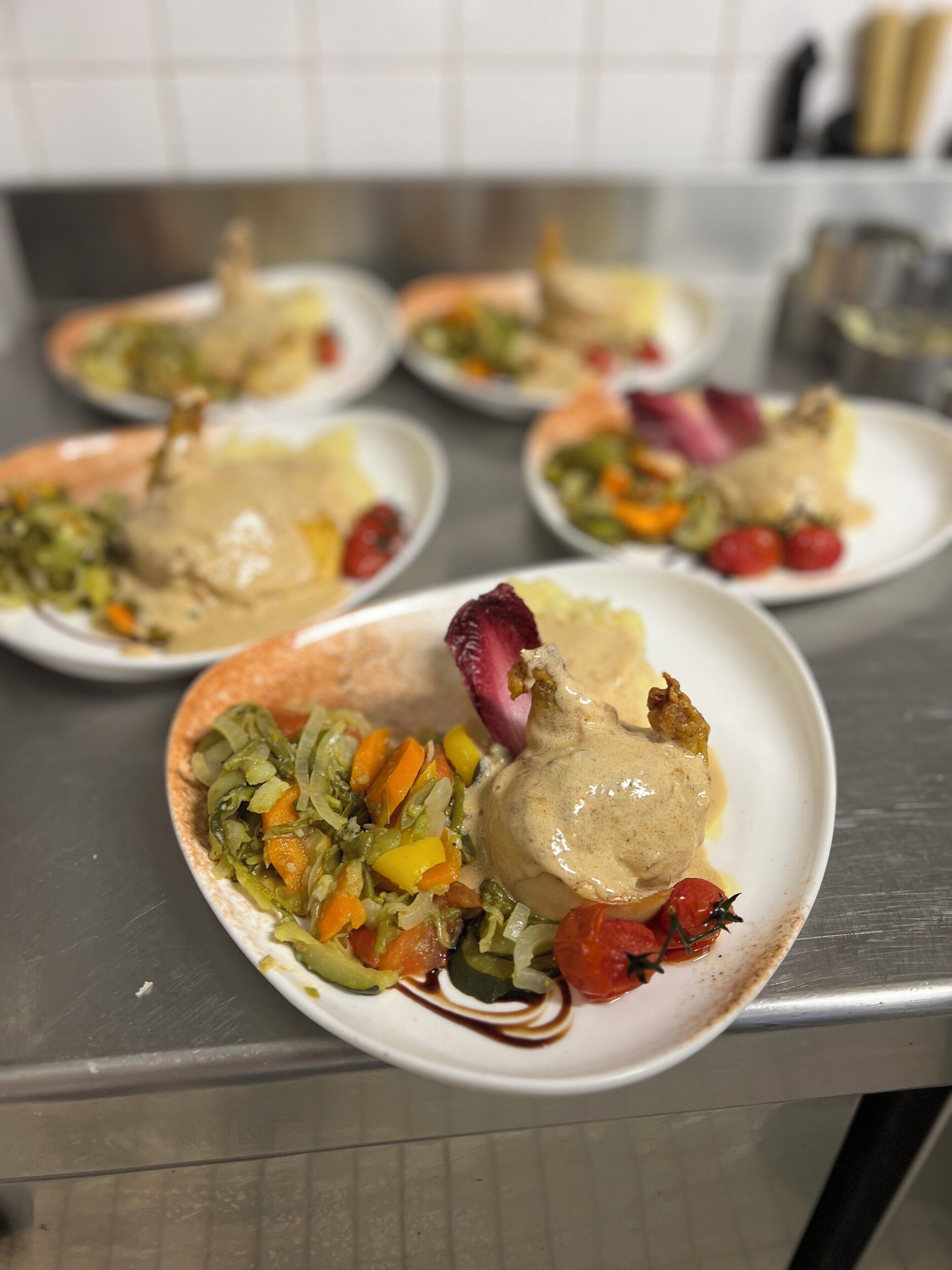 Une table à manger avec des assiettes remplies de nourriture, notamment un plat principal nappé d’une sauce crémeuse et accompagné de légumes.