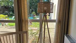 A room with a wooden chair, a floor lamp, and a view of a garden through large windows.