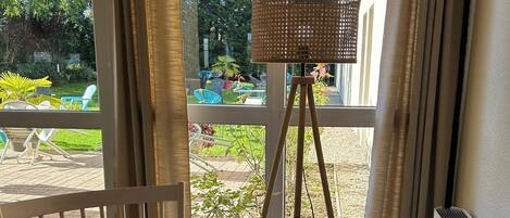 Une pièce avec une chaise en bois, un lampadaire et une vue sur un jardin, visible à travers de grandes fenêtres.