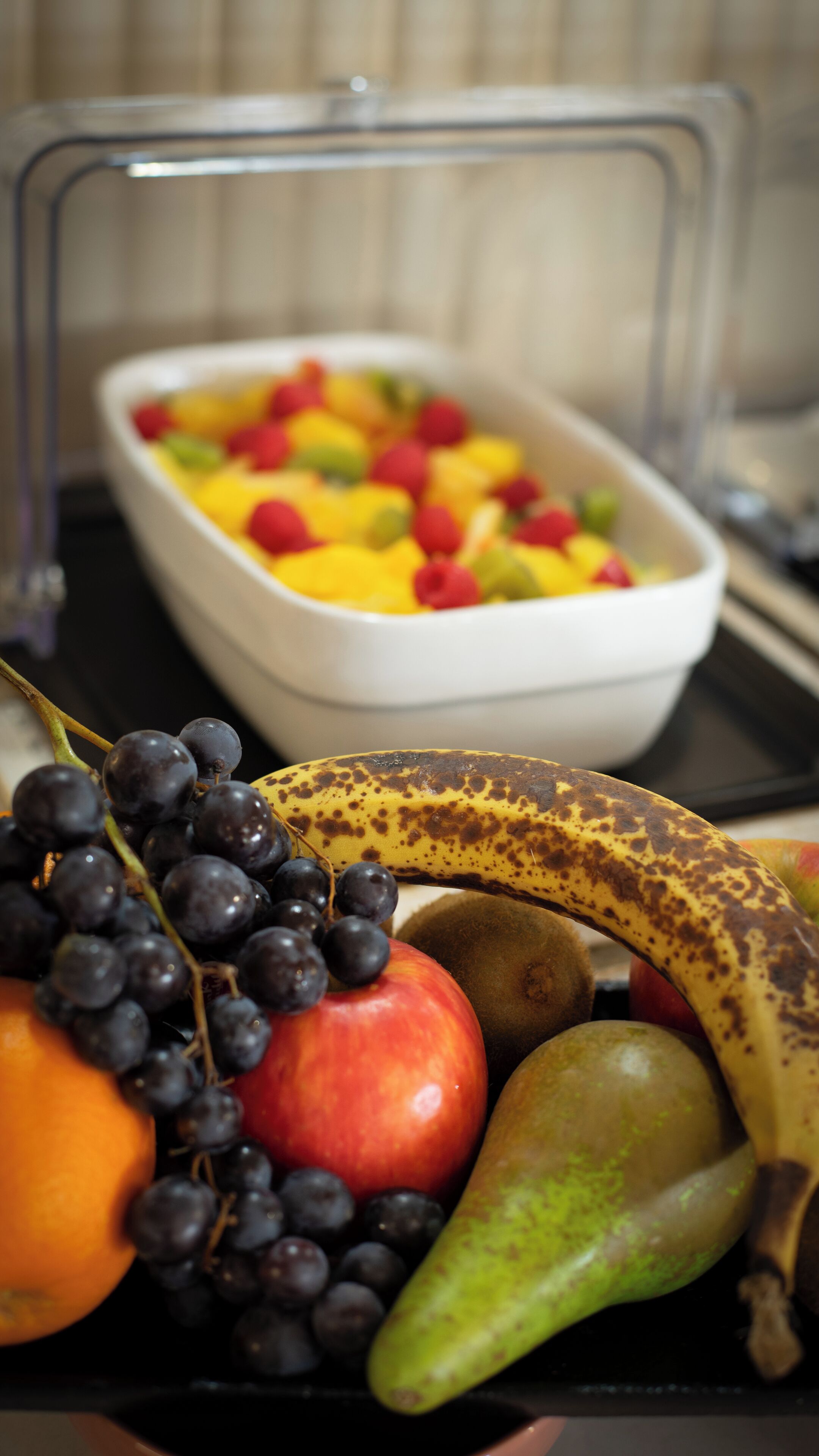 Un cuenco de frutas con uvas, una manzana, un plátano y un kiwi.