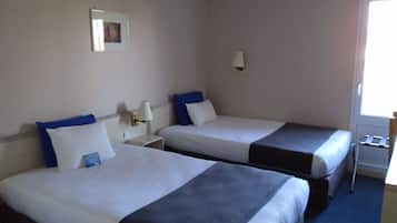 Habitació d'hotel amb dos llits, cada un amb roba de llit blanca i almoades blaves, una taula de nit amb una làmpada, i una finestra amb vista.