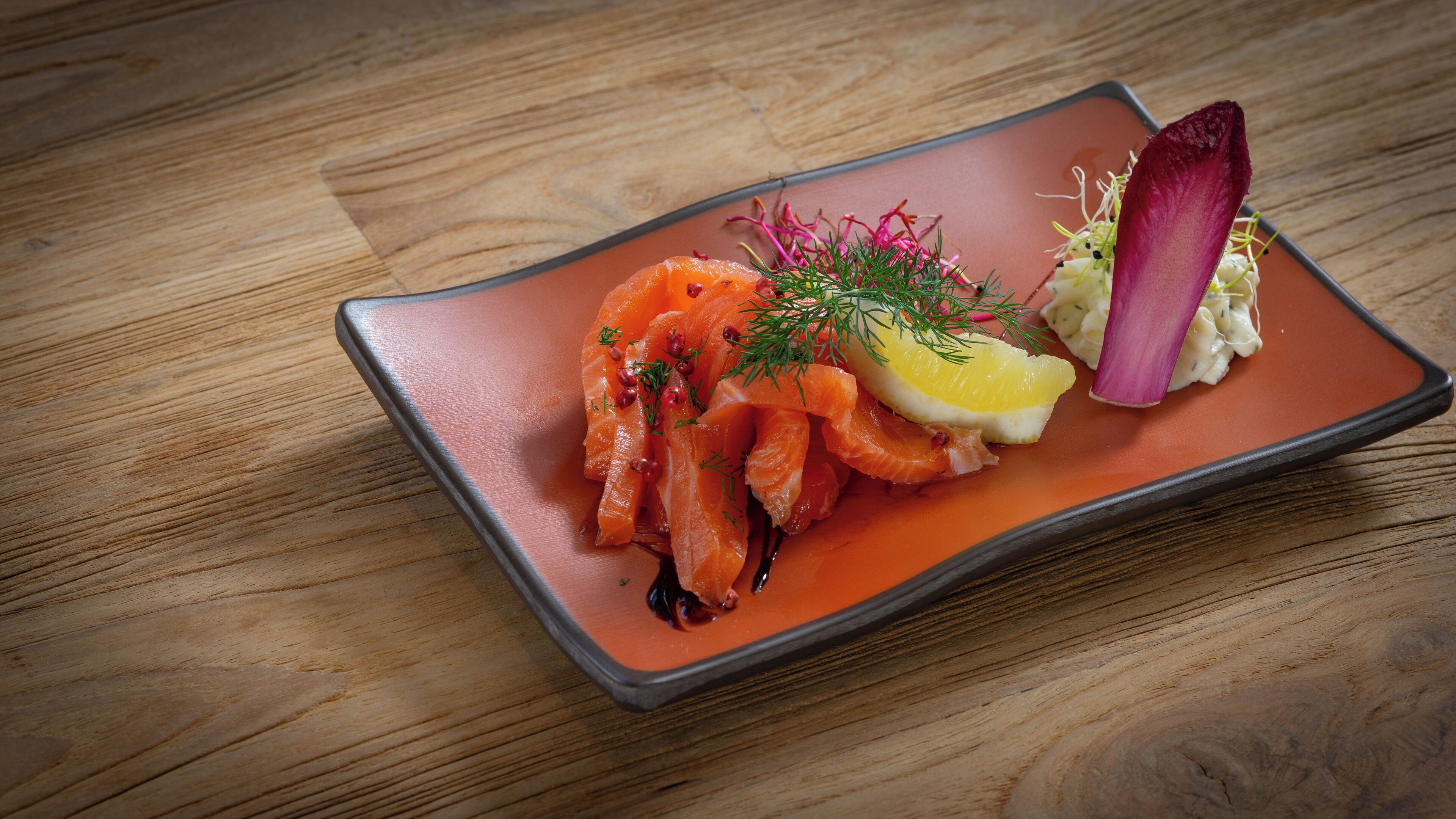 A rectangular plate with salmon, lemon, and a garnish on a wooden table.