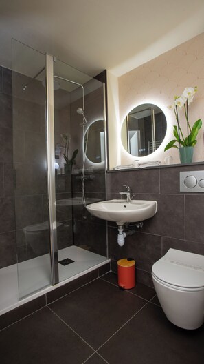Enjoy a refreshing shower in the bathroom, featuring a glass-enclosed shower, pedestal sink, and round mirror.