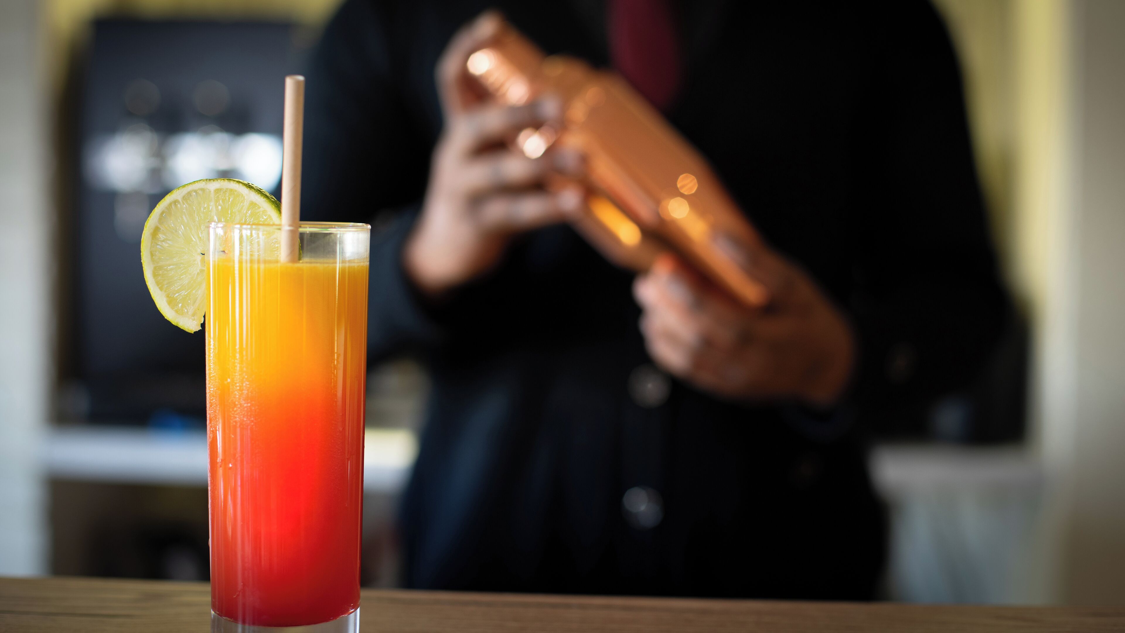 Ein Cocktail mit Limettenscheibe und Strohhalm in einem hohen Glas, auf einer Holzbodenfläche platziert.