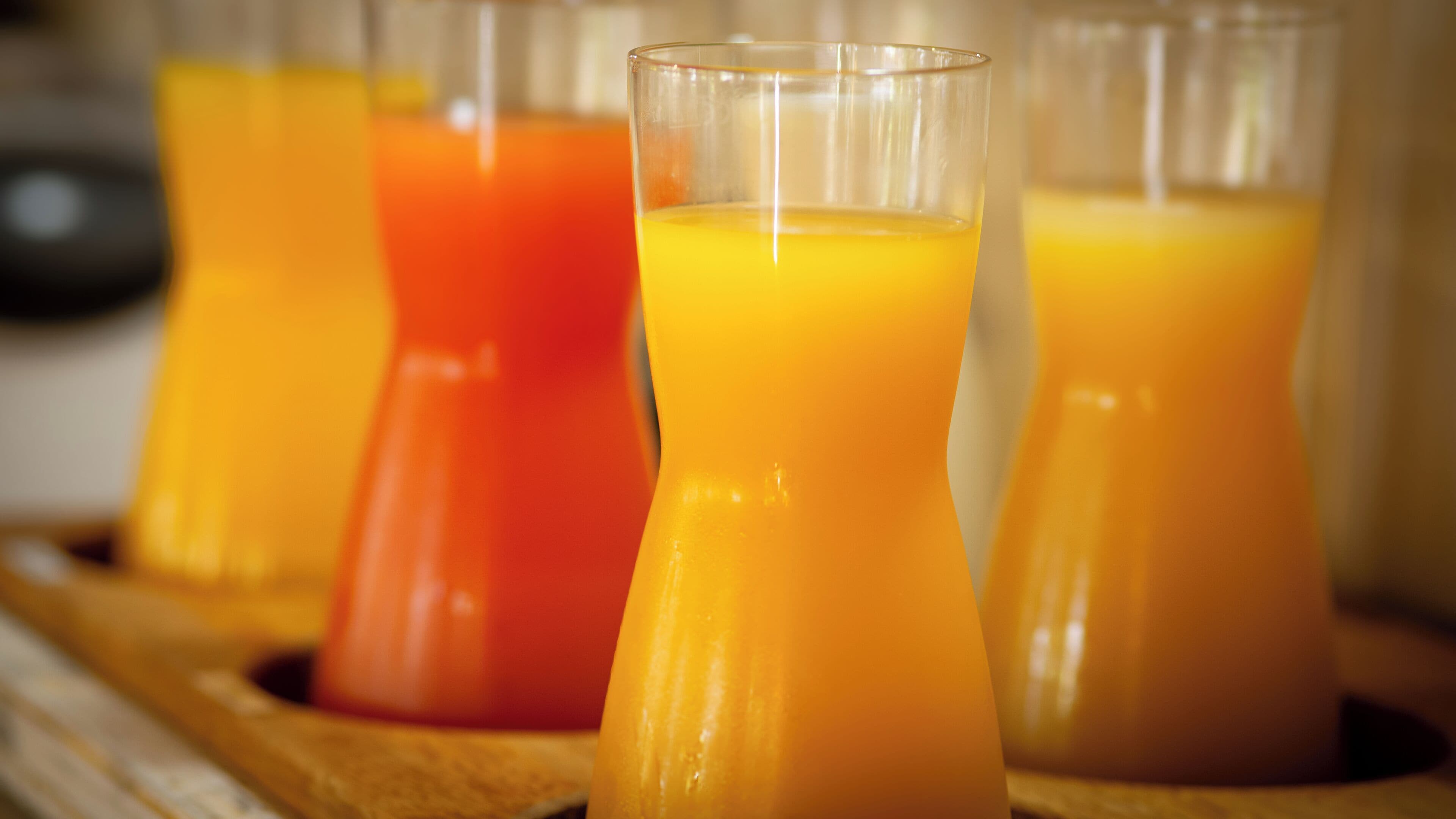 Quatro copos de suco de laranja em um tabuleiro de madeira.