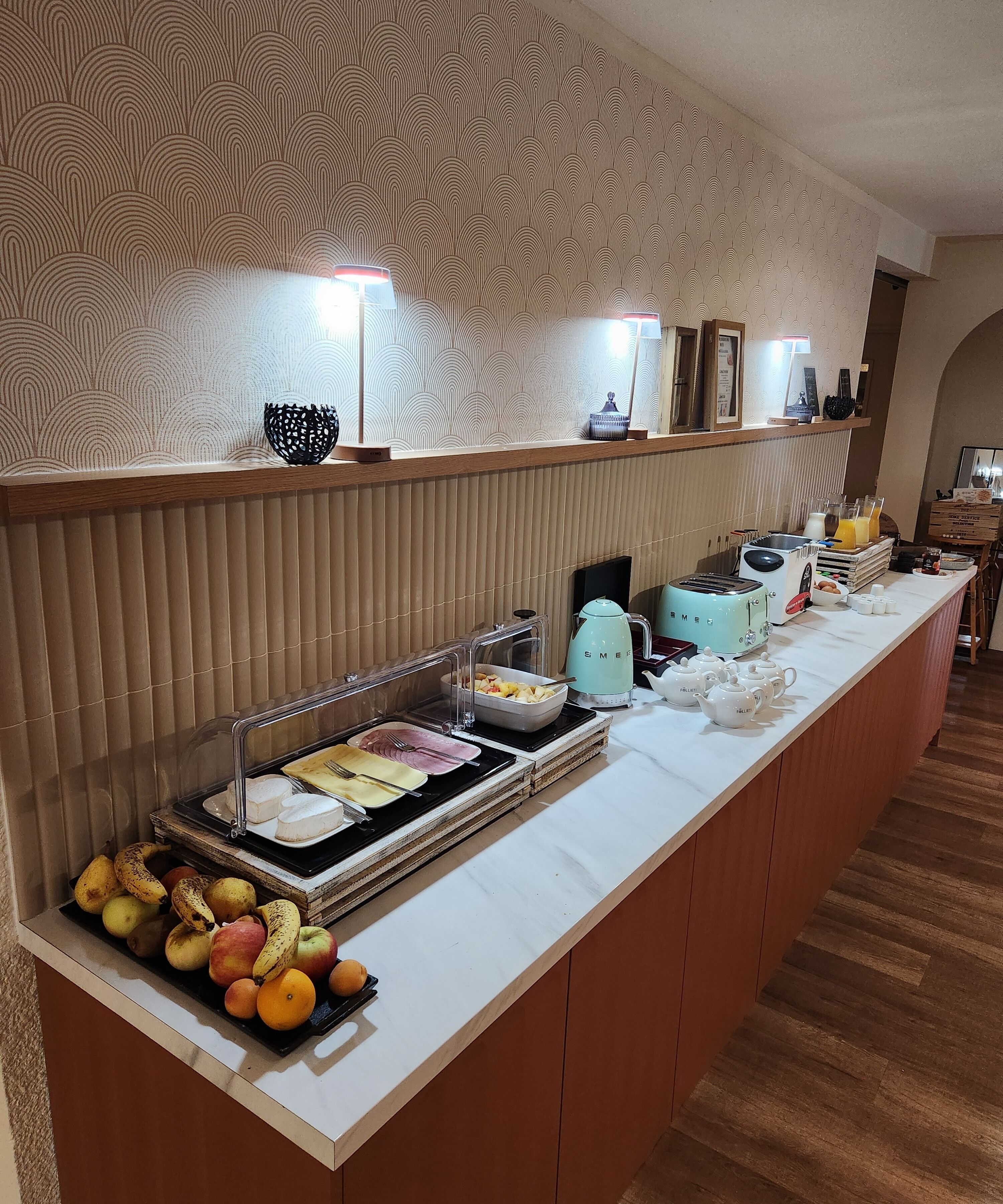 Mesa de buffet con varias frutas, un tostador y una tetera.