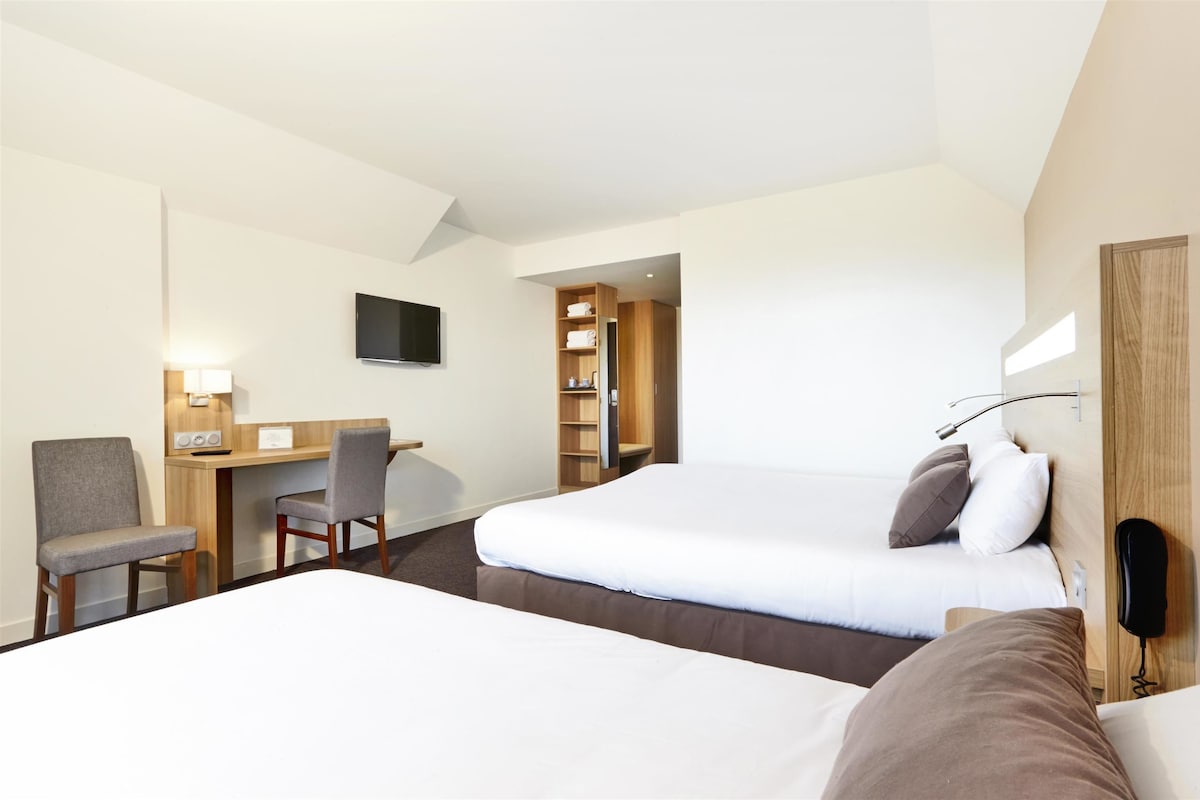 Una habitación de hotel con dos camas, un escritorio, una silla, un televisor y un teléfono.