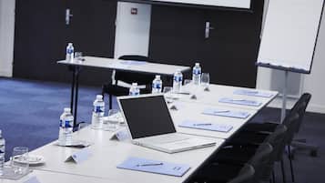 Un salón de conferencias con una larga mesa, portátiles, botellas de agua y tarjetas de identificación.