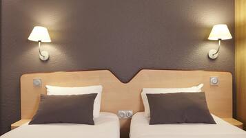 A hotel room with two beds, each with a pillow and a nightstand. There are wall-mounted lamps on either side of the beds.