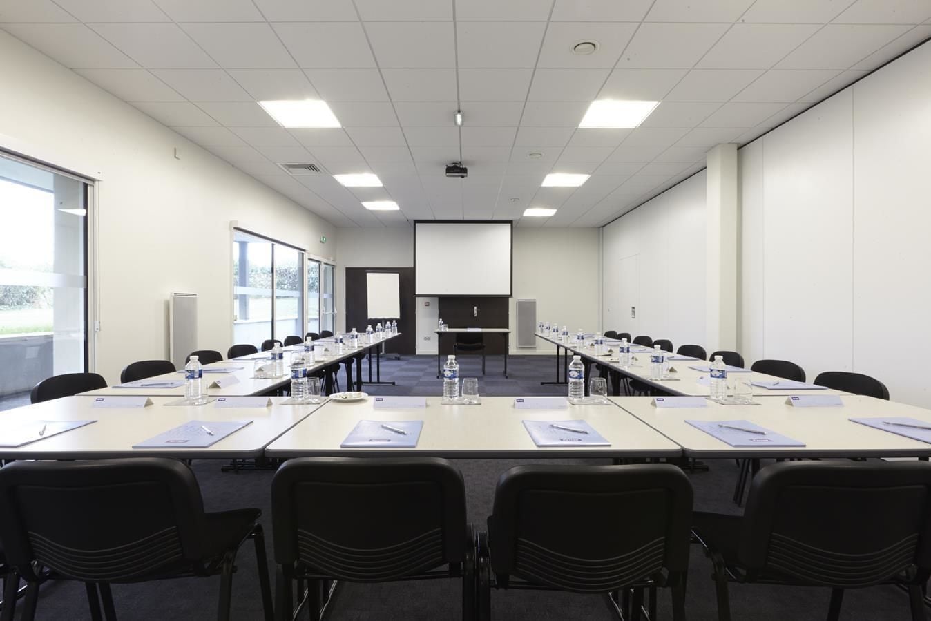 Un salón de conferencias con una larga mesa, sillas, botellas de agua y placas de identificación.
