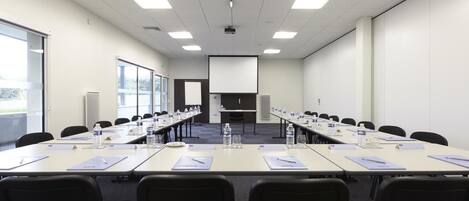 Un salón de conferencias con una larga mesa, sillas, botellas de agua y placas de identificación.