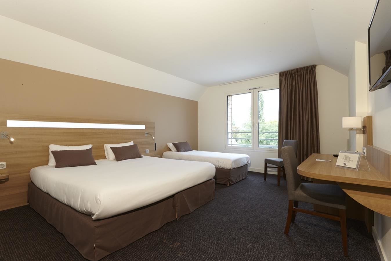 A hotel room with two beds, a desk, a chair, and a large window with curtains.