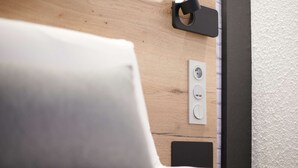 A bed with a white pillow, a wooden headboard, and a power outlet on the wall.