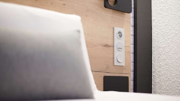A bed with a white pillow, a wooden headboard, and a power outlet on the wall.