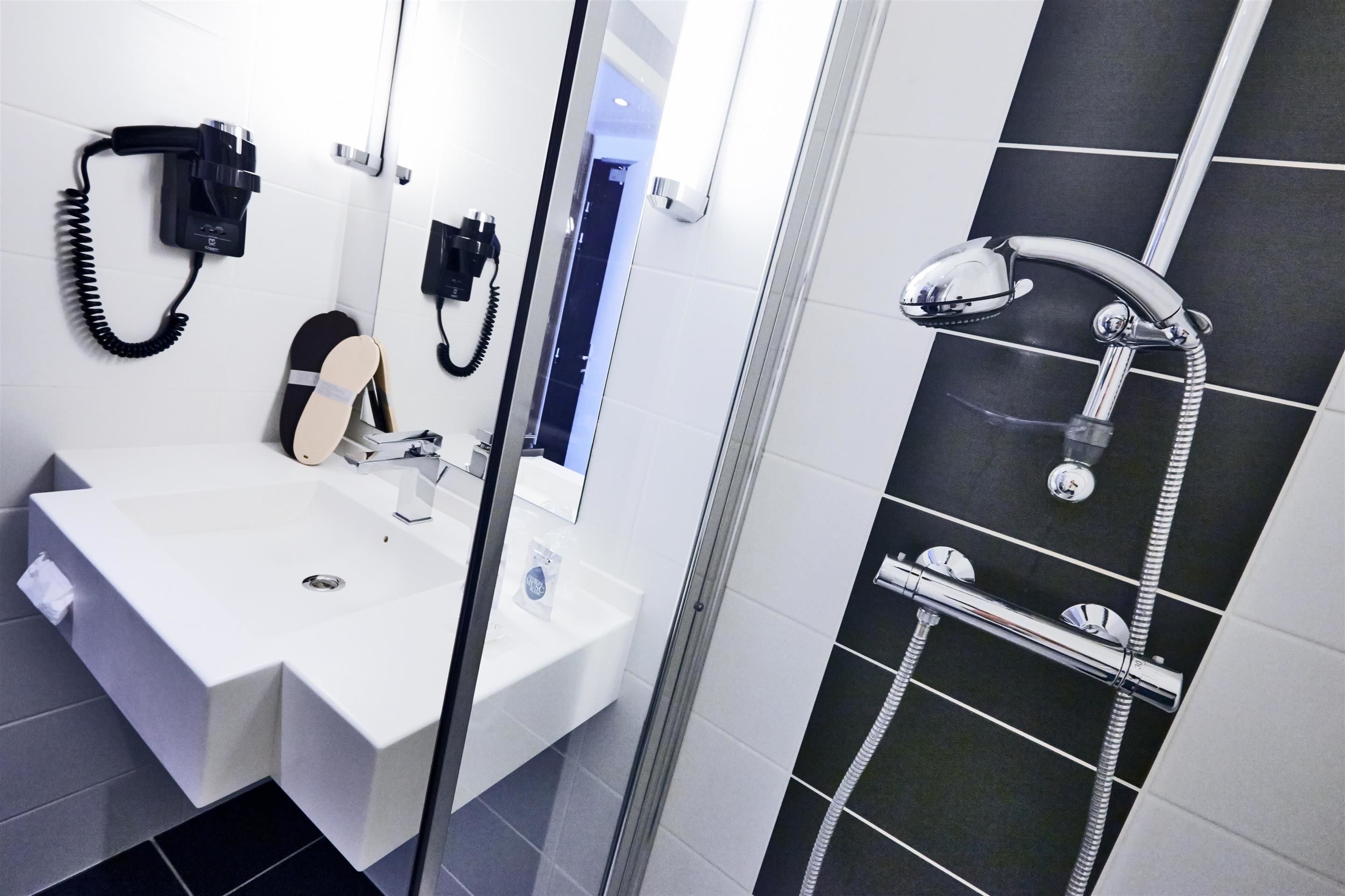 Un baño moderno con un lavamanos blanco, un espejo, un cabezal de ducha de mano y un teléfono instalado en la pared.