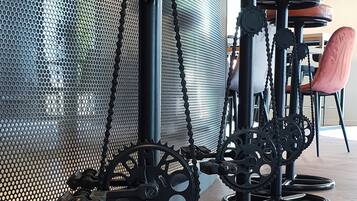 A row of bar stools with black metal frames and wooden seats, positioned in a room with a wooden floor and a mesh partition in the background.