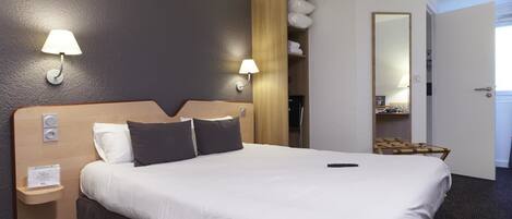 A hotel room with a large bed, two bedside lamps, a wooden headboard, a small bedside table, and a mirror.