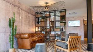 A modern lounge area with a leather sofa, a wooden chair, a round table, and a cactus plant. - Kyriad Laval (Laval)