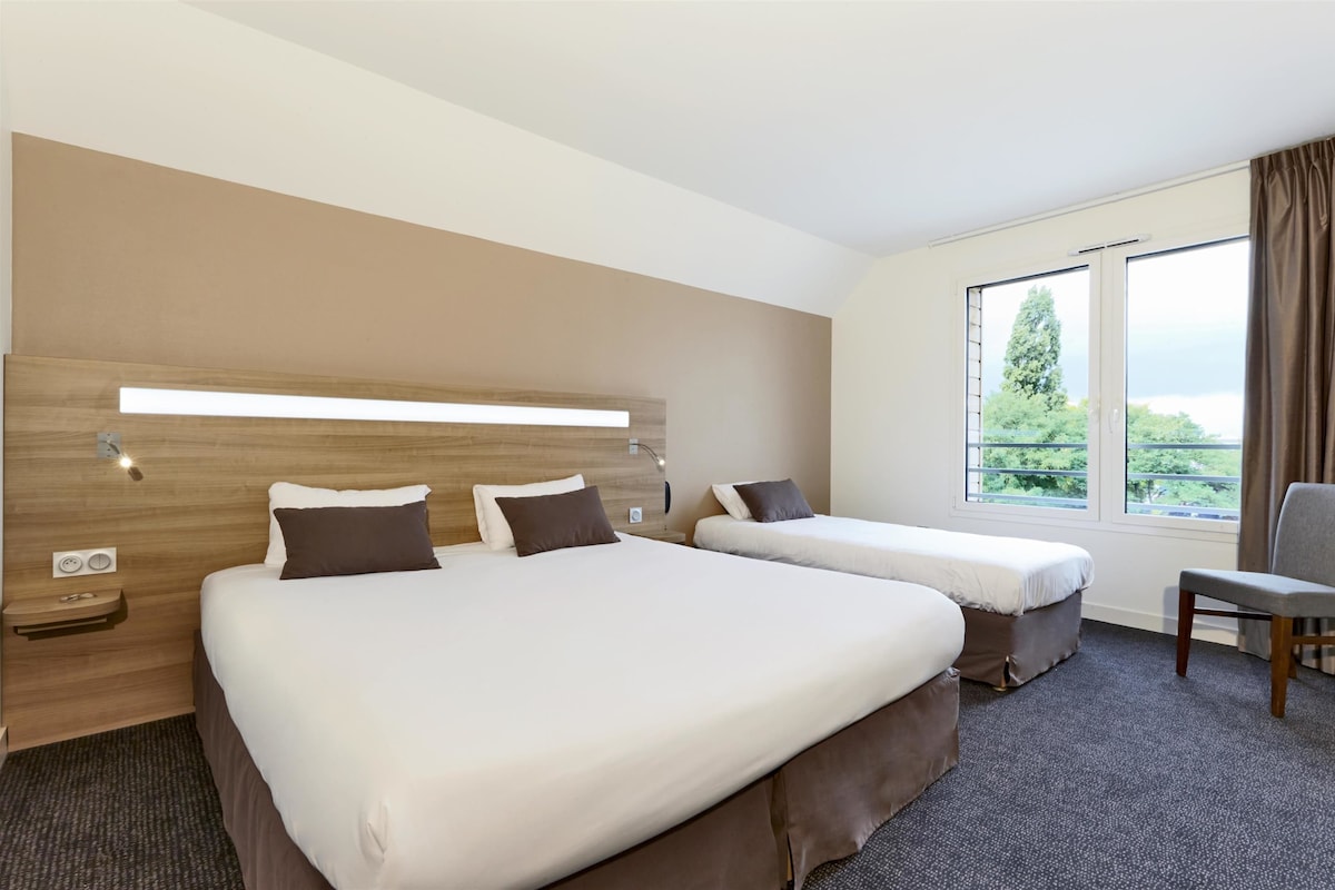 A hotel room with two beds, a large window with a view, a desk, and a chair.