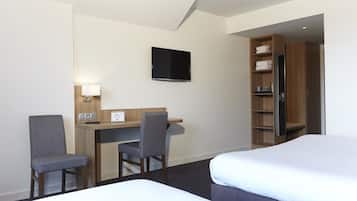 Une chambre d’hôtel avec deux lits, un bureau avec une chaise, un téléviseur fixé au mur et une armoire.