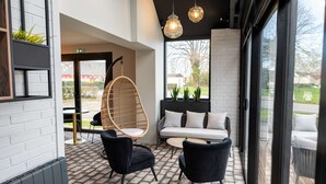 A modern interior with a black sofa, two black chairs, a hanging rattan chair, and a large window offering a view of the outdoors.