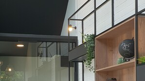 A modern interior with a black and white color scheme, featuring a seating area with a sofa and chairs, a wooden shelf unit with decorative items, and hanging pendant lights. - Kyriad Laval (Laval)