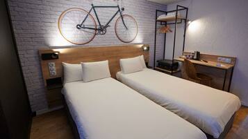 Habitación de hotel con dos camas individuales, cabecero de madera, bicicleta fijada a la pared, escritorio con silla y perchero.