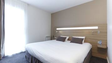 Habitación de hotel con una cama grande, una mesita de noche con una botella de agua y una lámpara fijada a la pared.