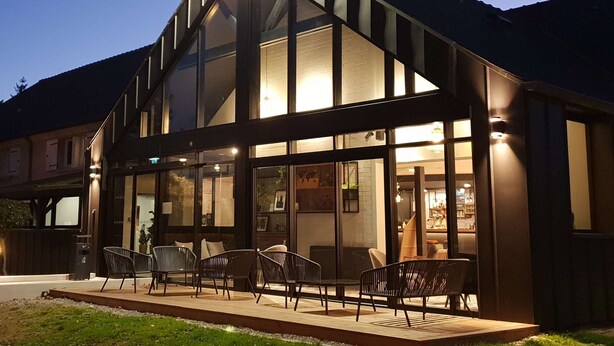 A modern building with a large glass facade, outdoor seating area with chairs, and a well-lit entrance. - Kyriad Laval (Laval)