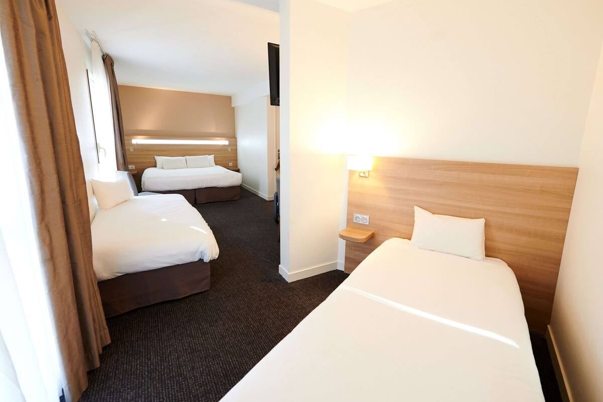 Habitación de hotel con dos camas, una mesita de noche con lámpara y cabecero de madera.