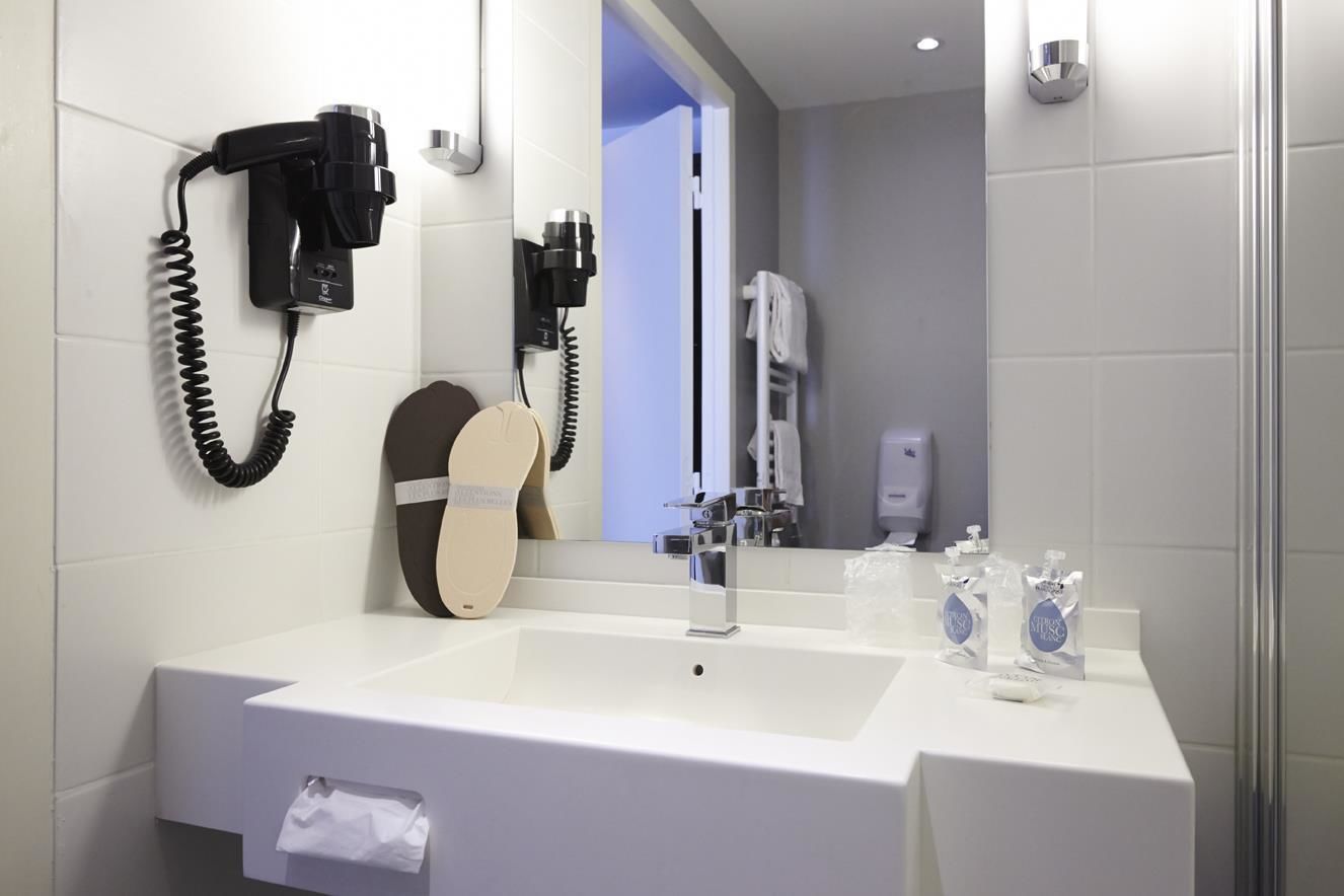 Un baño moderno con lavamanos blanco, un secador de pelo montado en la pared y un espejo.