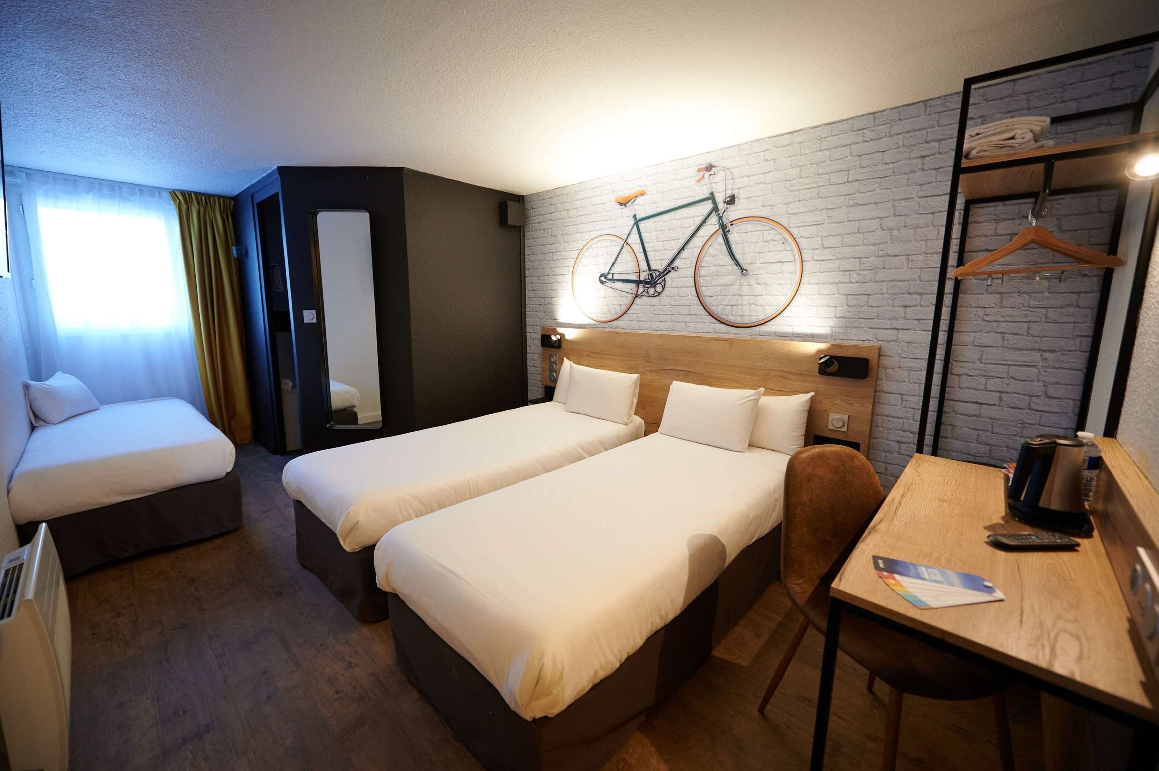 Habitación de hotel con dos camas, una mesa de madera, una bicicleta colgada en la pared y un perchero.