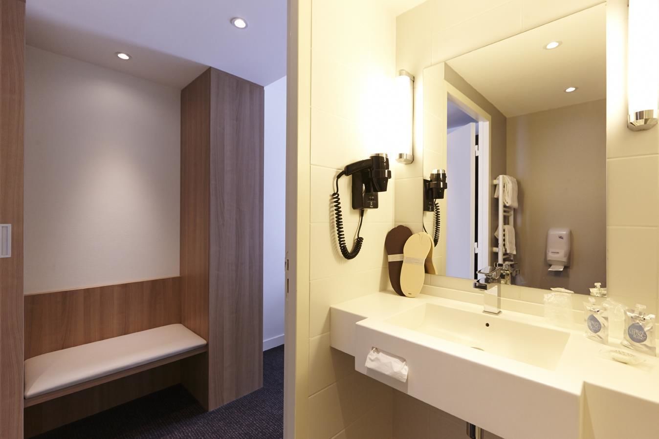A modern bathroom with a bench, a hairdryer, and a mirror.