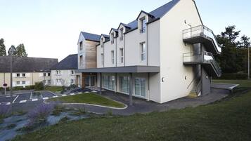 A modern multi-story building with a flat roof, large windows, and a covered entrance area.