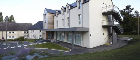 A modern multi-story building with a flat roof, large windows, and a covered entrance area.