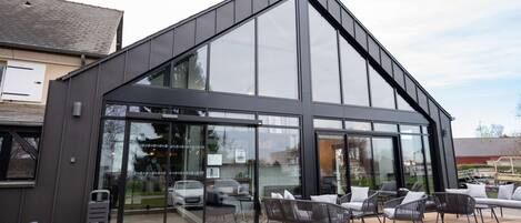 Un bâtiment moderne doté de grandes fenêtres, d’un toit en pente et d’un espace extérieur aménagé pour s’asseoir.