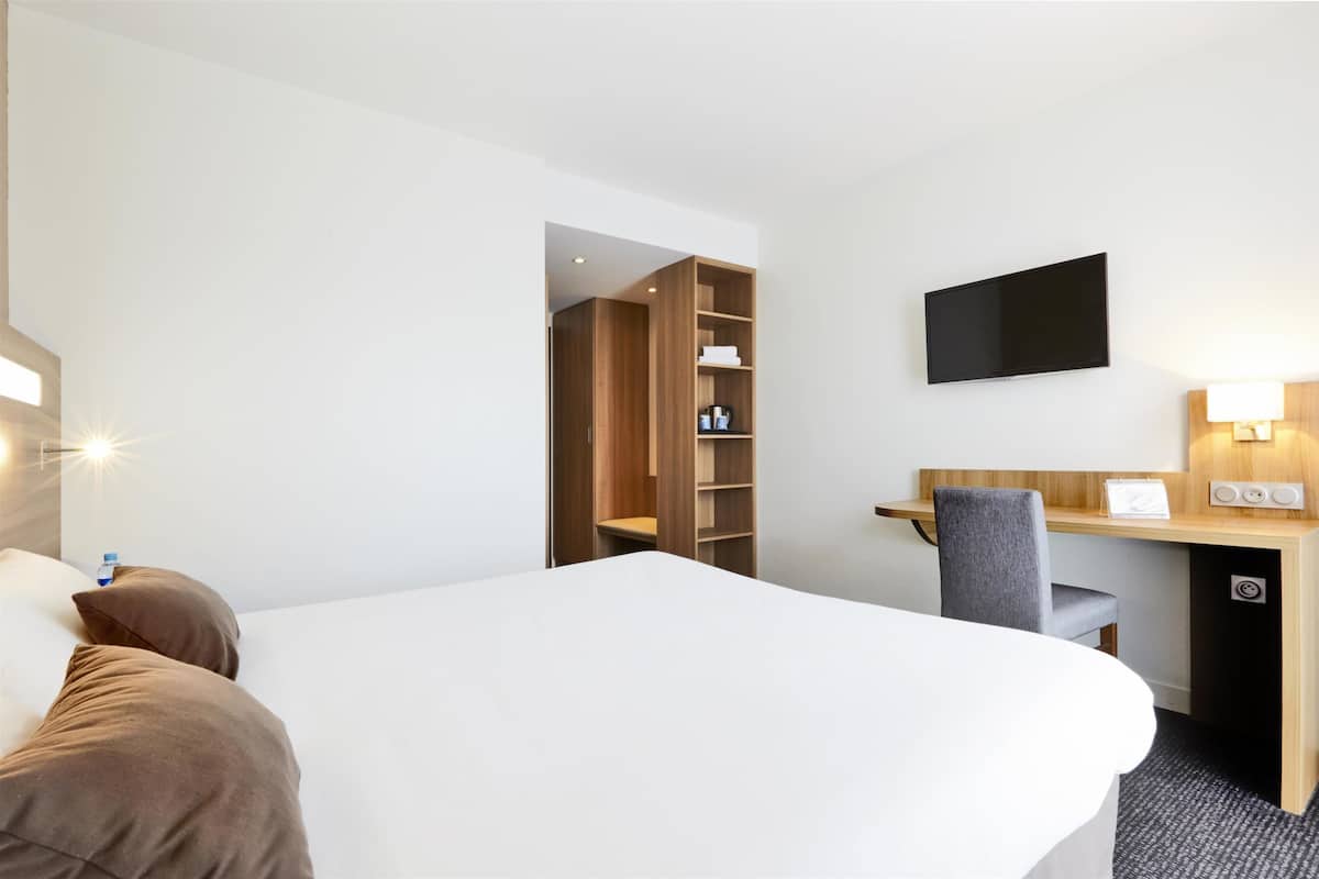 Habitación de hotel con cama, escritorio con silla, televisor en la pared y armario.