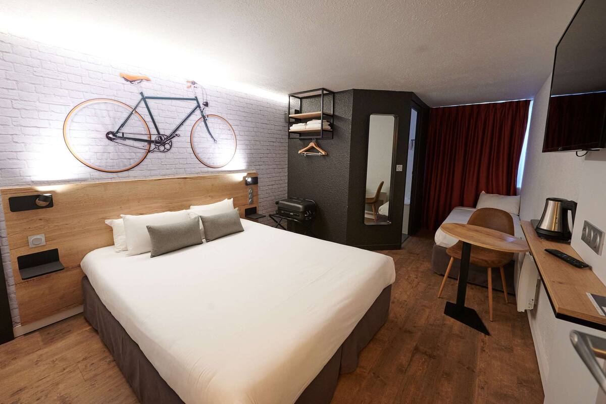 Una habitación de hotel con una cama grande, un cabecero de madera, una bicicleta colgada en la pared, un escritorio con una silla y un televisor.
