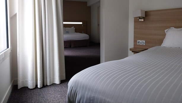 A hotel room with a large bed, a nightstand, a wooden headboard, and a window with curtains.