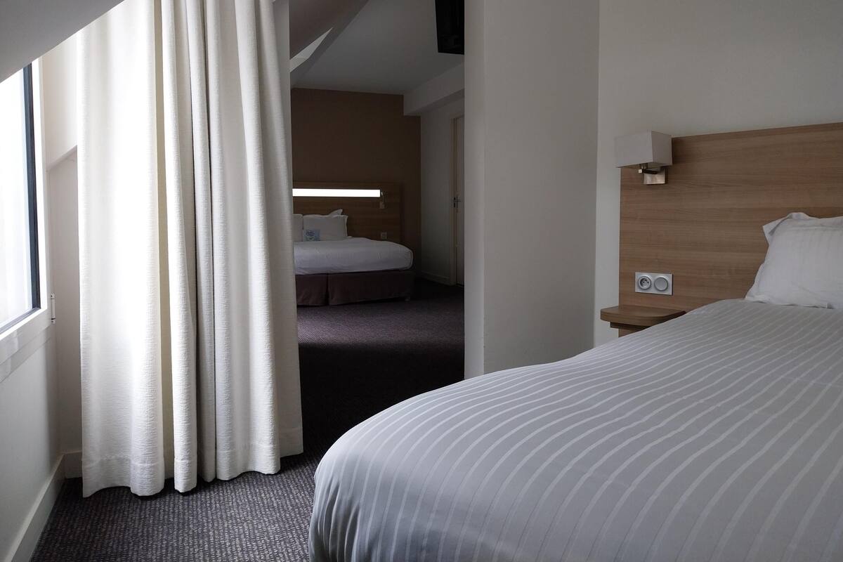 Una habitación de hotel con una cama grande, una mesita de noche, un cabecero de madera y una ventana con cortinas.