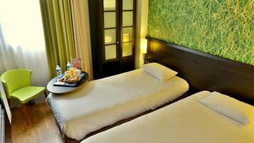 Habitación de hotel con dos camas, una mesita con desayuno, una silla verde y una pared con diseño que imita hierba.