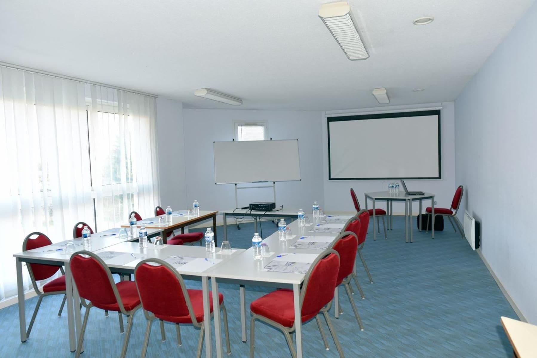 Un salón de conferencias con una pizarra, pantalla de proyector y una mesa con sillas.